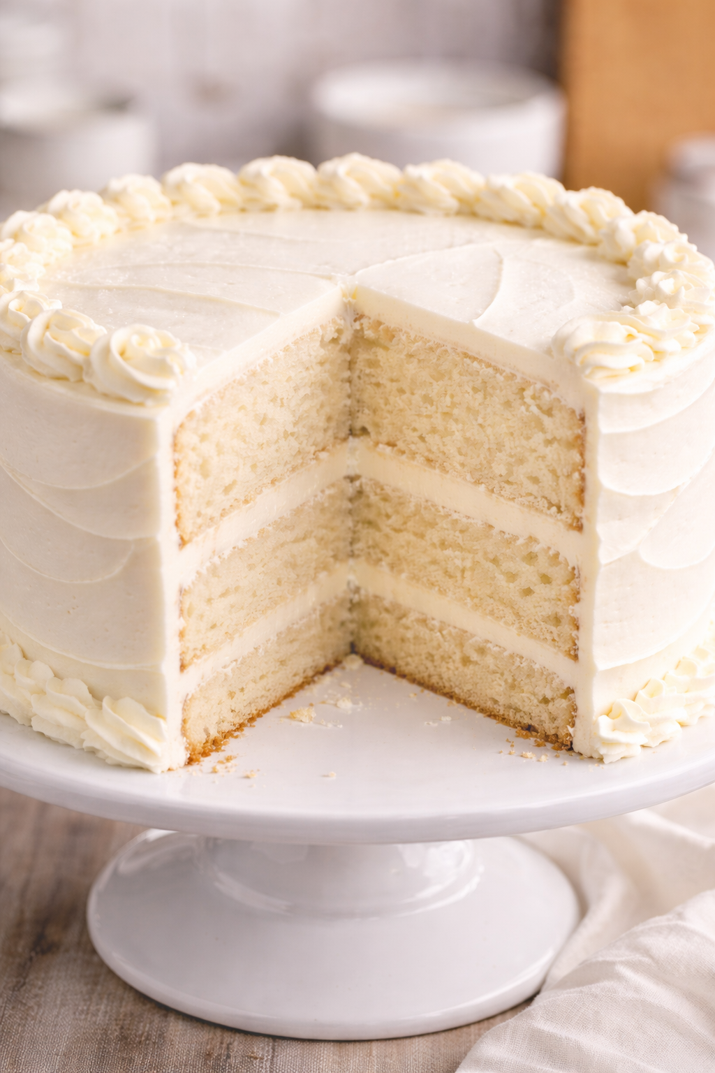 Three-layer vanilla cake with white frosting on a white cake stand.